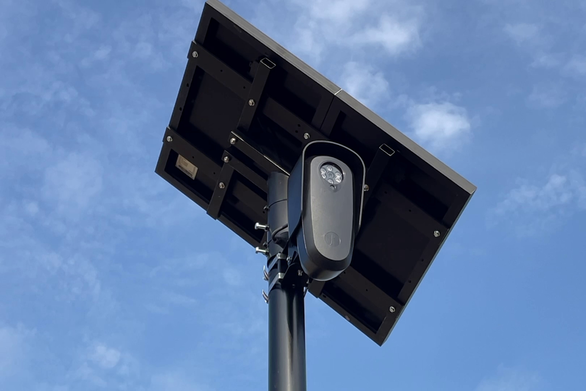 A Flock Safety ALPR camera mounted on a black pole against a blue sky
